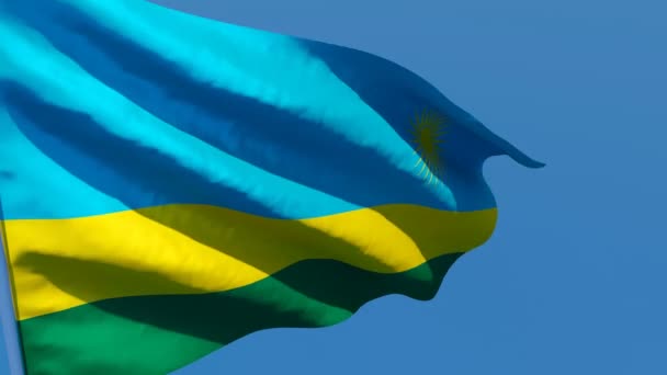 Rwandas nationella flagga fladdrar i vinden mot en blå himmel — Stockvideo