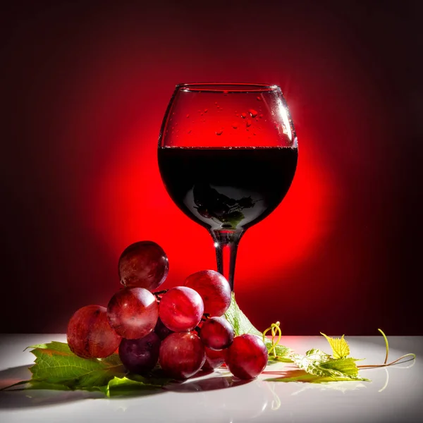 serving glass of red wine and grapevine with green leaf