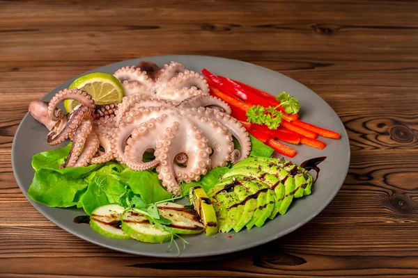 octopus served with sliced avocado, lettuce, red pepper, lime, cucumber and sprig of pea leaves on plate, healthy organic food