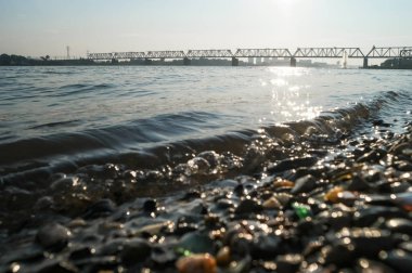 Ob nehrinin kıyısından Transsib 'in demiryolu köprüsü manzarası. Bulanık nehir çakıl taşları görünümlü köprüye seçici odaklan.