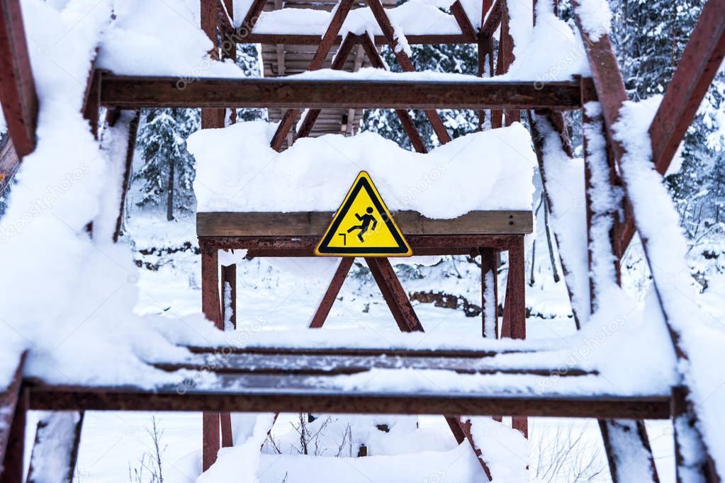 Warning sign: caution, possible fall from height on old bridge in the park.