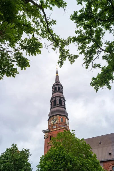 Hamburg, Almanya. St. Katharinen Kilisesi 'nin saatli çan kulesi. Ağaç dalları tarafından çerçeve olarak çerçevelenmiş tapınak kulesi görüntüsü.