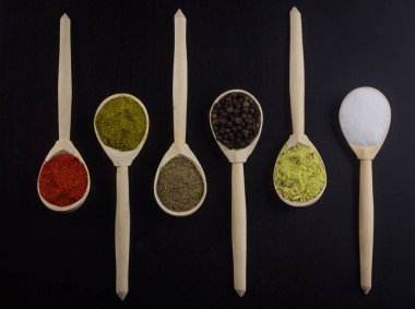 Aroma baharat koyu arka plan üzerinde farklı tipleri ile altı kaşık. Burada bulabilirsiniz: tuz, toz biber, Mısır, kırmızı biber ve iki tür karışık baharat biber