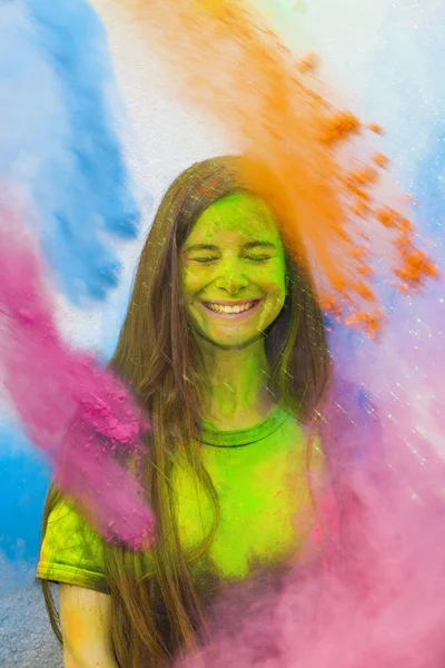 Young cheerful girl under explosion of colored powder at Holi colors (paints) party. Freeze motion (stop motion) of color powder exploding or throwing colour powder. Multicolored glitter explosion.