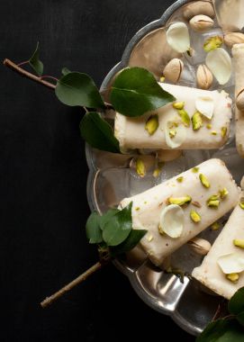 Pista kulfi, Hint dondurma plaka hizmet buz küpleri, Antep fıstığı, gül yaprakları, siyah arka plan, üstten görünüm üzerinde yeşil yaprakları ile ağaç dalları üzerinde. Geleneksel Rajasthani Hint Mutfak.