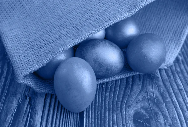 Барвисті великодні яйця на дерев'яному тлі в мішковині, тонований трендовий класичний синій колір року 2020 — стокове фото