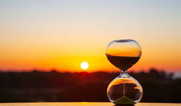 Zandloper bij zonsondergang of zonsopgang op een wazige achtergrond, als herinnering aan de verstreken tijd — Stockfoto