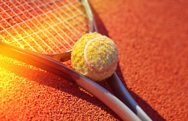 Single tennis racket on a orange sand court with a tennis ball on a lighted background. Close-up — Stock Photo, Image