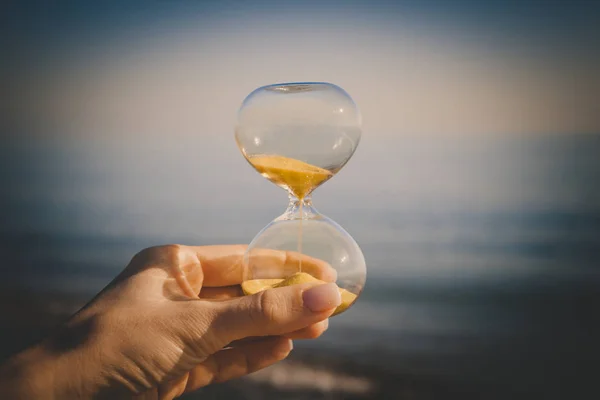 Sand in der Sanduhr und Sand auf dem Meer, Zeit in den Händen eines jungen Mädchens, das Konzept fallender Sandkörner in einer Glasflasche — Stockfoto