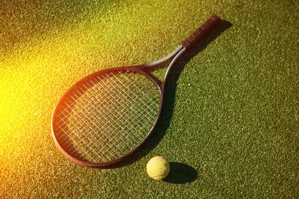 Tennis racket and yellow ball on the court with green grass and sunlight — Stock Photo, Image