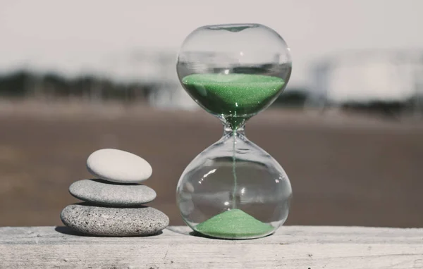 Pyramid of three stones nearby and an hourglass with green sand. Vacation time concept