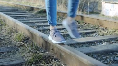Tırabzanlar üzerinde yürüyen kotlu bir kızın bacaklarının yakın çekimi. Hiç tren yok..