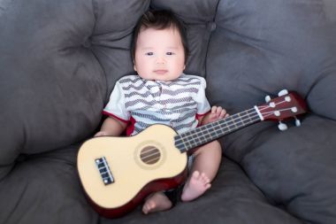 Mini gitar ile yumuşak kanepede oturan bebek güzel. bebekler müzisyen. Çocuklar için müzik becerilerini uygulama. müzik ve çocuklar. görüntü arka plan, nesneler, illüstrasyon, makale ve moda için.