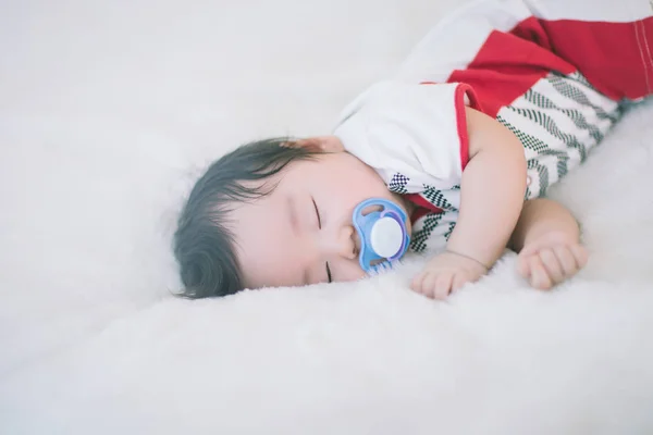 かわいい赤ちゃんがおしゃぶりを吸うと柔らかい白いカーペットの上で寝ています — ストック写真