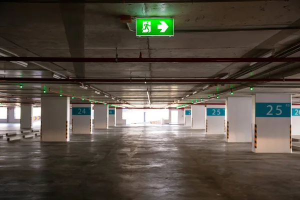 empty indoor car park and fire exit label, hang on the ceiling. many space parking garage in the building. building safety standard. image for background, copy space, objects, illustration and article