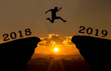 Genç bir adam hill siluet akşam renkli gökyüzü boşluğu üzerinde 2018 ve 2019 yılları arasında güneş üzerinde ve üzerinden atlamak. mutlu yeni yıl 2018.