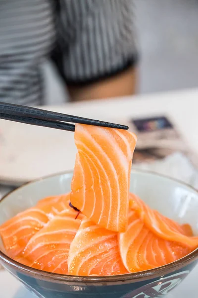 Close up salmon slice took by chopsticks. salmon topped by fresh salmon served with wasabi and soy sauce, donburi rice. image for background, copy space, decorate and menu list.