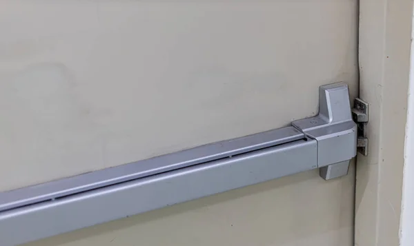 Emergency fire exit door. Closed up latch and rusty door handle of emergency exit. Push bar and rail for panic exit. Open one way door.  steel of handle for the white door fire exit