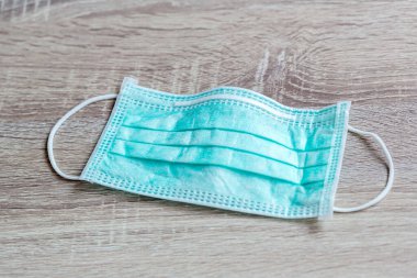 Protective face mask on wood table. Typical 3-ply surgical mask to cover the mouth and nose. Procedure mask from bacteria. Protection concept. Surgical mask with rubber ear straps.