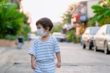 Child wearing a protective face mask on a city street with air pollution. Facial hygienic mask for Safety outdoor environmental awareness concept And protect disease virus against germs dustpm2.5