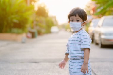 Child wearing a protective face mask on a city street with air pollution. Facial hygienic mask for Safety outdoor environmental awareness concept And protect disease virus against germs dustpm2.5