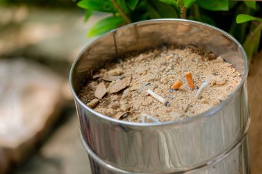 Kum kül tablasında bir sürü sigara koçanı. Sigaraların geri kalanı kül tablasında. Kül tablasında kumun üzerinde bir sürü sigara izmariti vardır. Bir sigara sağlık için iyi değildir.. 