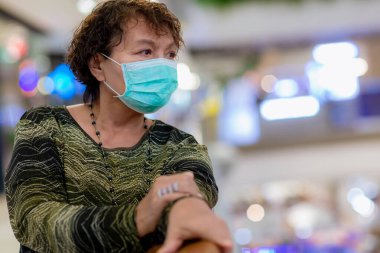 Kraliyet virüsüne karşı korunmak için Covid-19 maskeli yaşlı Asyalı kadın. Kirli hava dumanı yüzünden koruyucu maskeli Asyalı yaşlı kadın, PM2.5. Coronavirus yaşlı kadın ameliyat maskesiyle yürüyor.