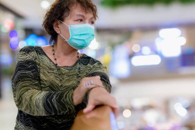 Kraliyet virüsüne karşı korunmak için Covid-19 maskeli yaşlı Asyalı kadın. Kirli hava dumanı yüzünden koruyucu maskeli Asyalı yaşlı kadın, PM2.5. Coronavirus yaşlı kadın ameliyat maskesiyle yürüyor.