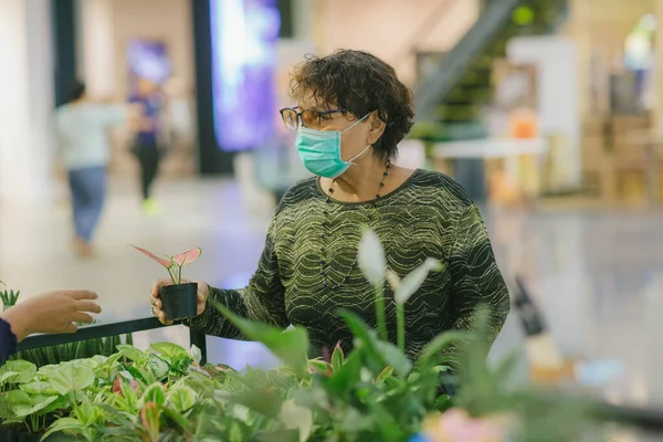 Asian old woman select buy plants. Old asian woman in a mask for COVID-19, for protection against the crown virus. Asian senior woman with protective mask because dirty air smog, PM2.5.