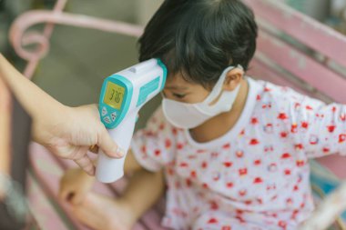 Hastanede sıcaklığı ölçen doktor. Anne evde kızıl saçlı alın termometresi olan bebek için ateşini ölçüyor.