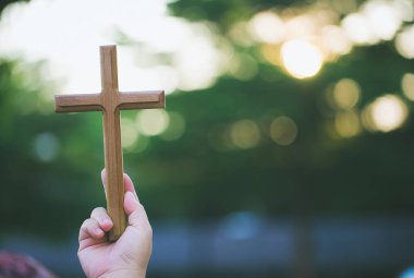 Bulanık bir arka planda ahşap bir haç tutan el.