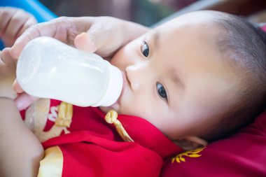 baby boy feeding her face with milk bottle