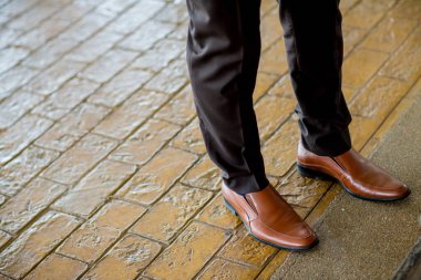 man's legs in a leather jacket and a black shoes on the street