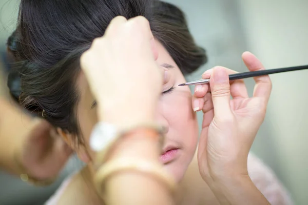 Beautiful bride applying wedding make-up by professional make-up artist on the wedding day.blur image of people at haircut shop.Women\'s haircut. hairdresser, beauty salon.