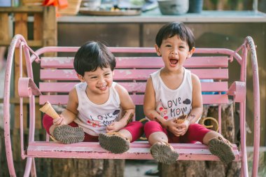 İkiz çocuk gülümsüyor ve mutlu salıncağa oturuyor. Kirli yüzlü ve mutlu dondurma yiyen ikiz çocuk. Tatlı dişli bir çocuk çikolata yer. Çikolata yiyen tatlı çocuk..