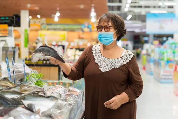 Old woman wearing a protective mask shopping during the pandemic. Emergency to buy list.food and supplies shortage. Protection measures while epidemic time. Preparation for a pandemic quarantine