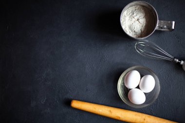 Yemek pişirme süreci. Un, bir tabakta üç yumurta, siyah mermer zemin üzerinde merdane ve iğne. Bir yazı için fotoğraf.