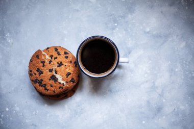 Siyah beton zeminde üç büyük kurabiye ve bir fincan kahve. Bir kurabiye iki parçaya ayrılır. Çikolatalı kurabiyeler. Yazı için görüntü