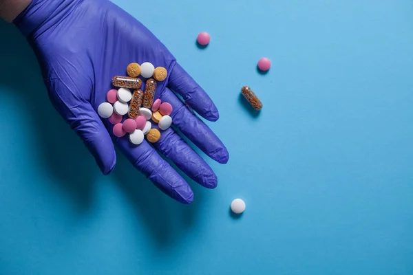Mavi eldivenli eller açık mavi arka planda bir avuç dolusu hap tutuyor. Asgari tıbbi konsept. Düz konum, üst görünüm, kopyalama alanı