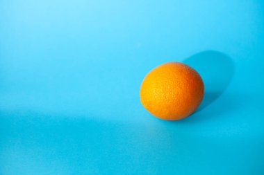 Bir portakal mavi arka planda yatıyor.