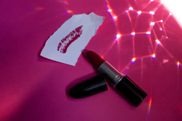 Red lipstick and smear on paper all on a pink background. Place for text. Flat lay