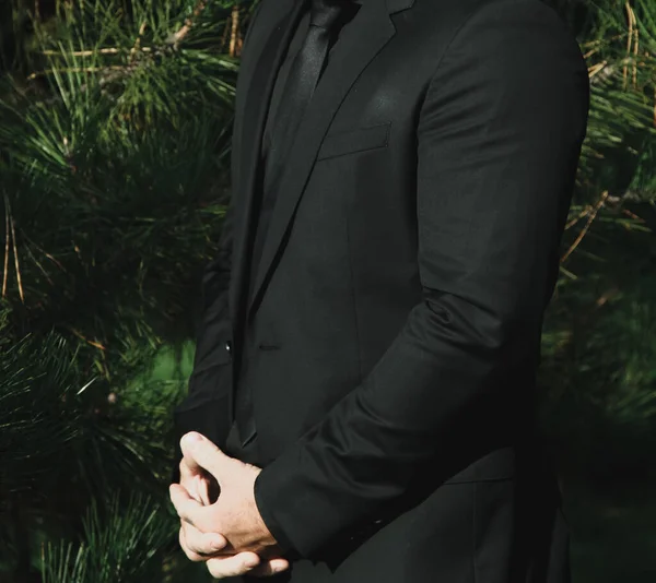 Siyah takım elbiseli güçlü bir adam Noel ağaçlarının arka planında. Doğadaki damat, düğün günü