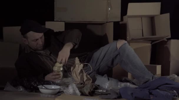 一个无家可归的中年男子拿了一卷面包和香肠开始吃饭 当你无家可归时 街上的褐色纸板箱就成了你的家 — 图库视频影像
