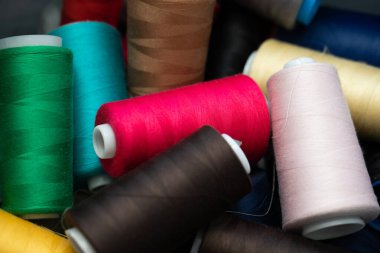 Dikiş makinesine yerleştirilmeye hazır bir kutuya rastgele dağılmış büyük bobinlerin farklı iplik renkleri.