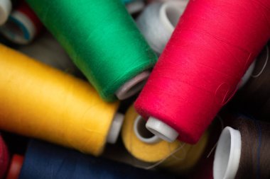 Dikiş makinesine yerleştirilmeye hazır bir kutuya rastgele dağılmış büyük bobinlerin farklı iplik renkleri.