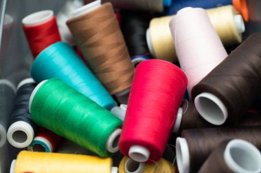 Dikiş makinesine yerleştirilmeye hazır bir kutuya rastgele dağılmış büyük bobinlerin farklı iplik renkleri.