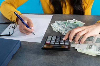 Masanın üzerinde hesap makinesi, tablet ve genç bayanın saydığı bir yığın kağıt para yatıyor. Masanın üstündeki kadın elleri büyük miktarda banknotları sayarken....