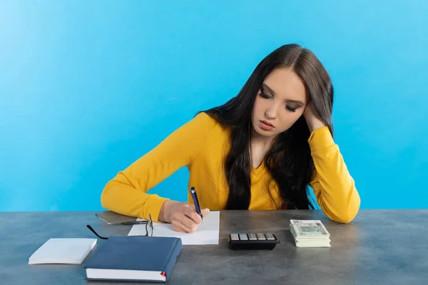 While counting money, a young woman uses a calculator and a tablet to check the stock exchange. A rich young girl counts money at home at her desk for her next major financial investment.