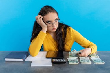Para sayarken, genç bir kadın borsayı kontrol etmek için bir hesap makinesi ve tablet kullanıyor. Zengin bir genç kız bir sonraki büyük yatırımı için masasında para sayıyor..