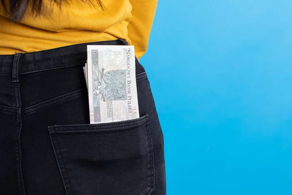 A cash file in the back pocket is a sign of financial wealth. A young woman inserts a bundle of paper banknotes into the back pocket of jeans.